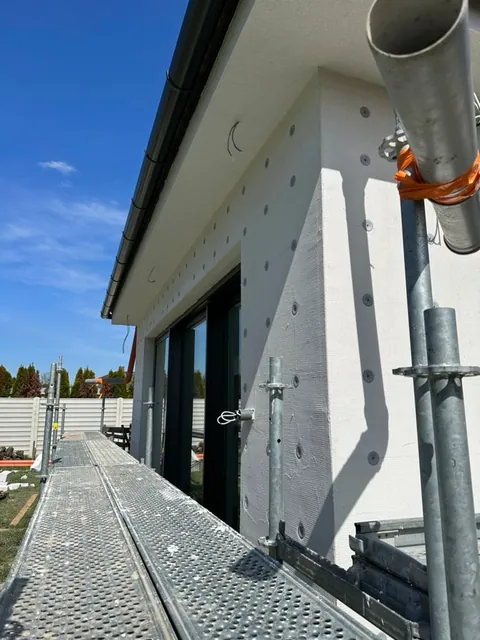 Detail rohu domu s polystyrénom a tanierovými hmoždinkami, v pozadí lešenie